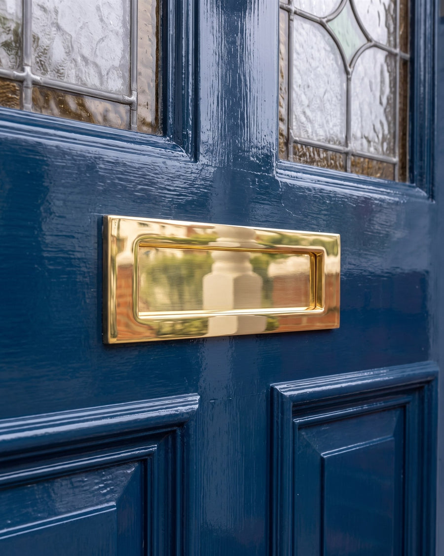 Polished brass Victorian letter plate on the middle rail of a glossy inky blue Edwardian door below the stained glass