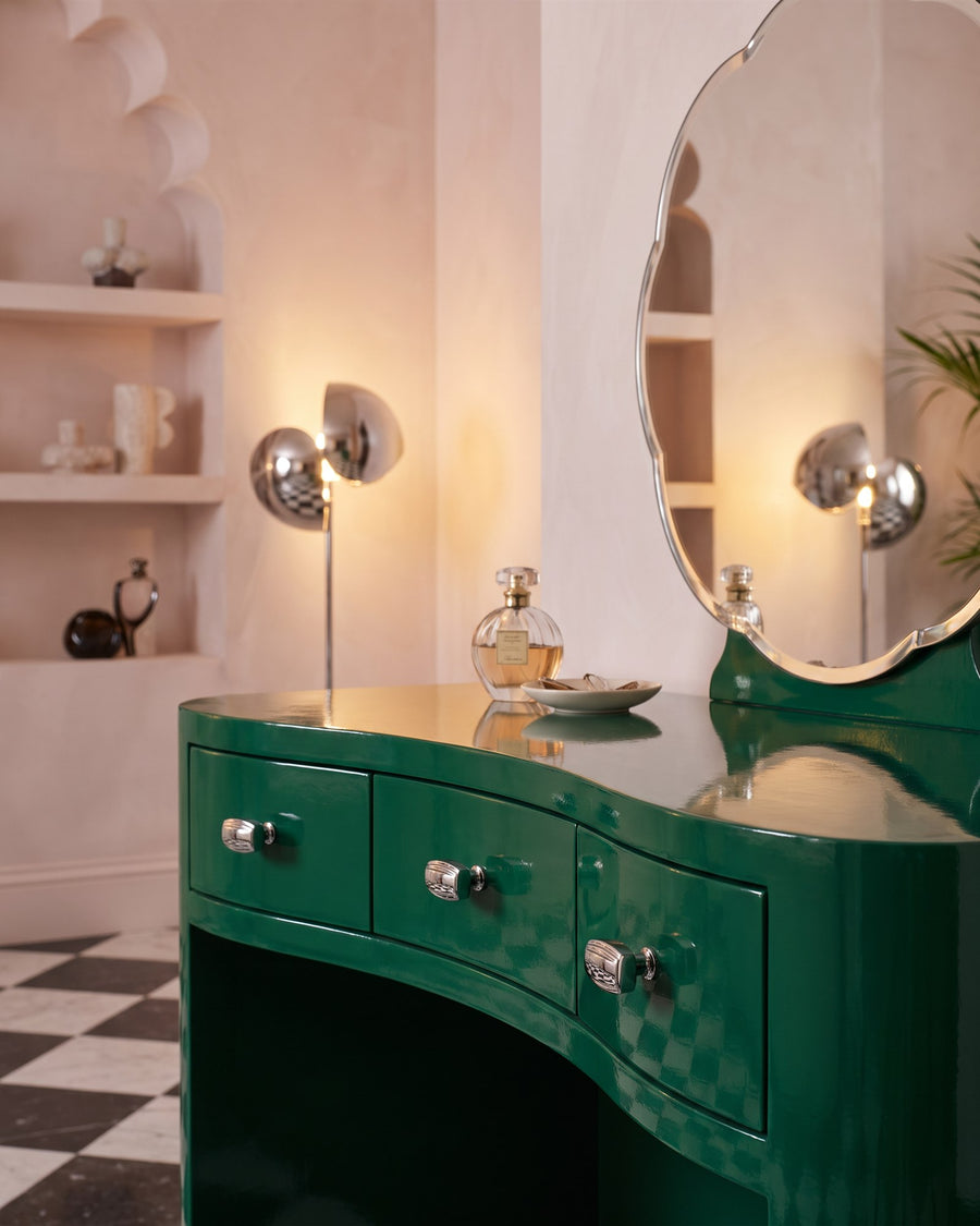 Polished chrome Art Deco cabinet knobs on a curved emerald lacquered dressing table with a scalloped mirror
