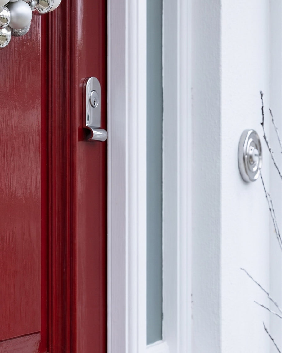 Polished chrome cylinder pull on the lock stile of a red door beside a white frame and side light, with a round chrome bell push on the white porch wall