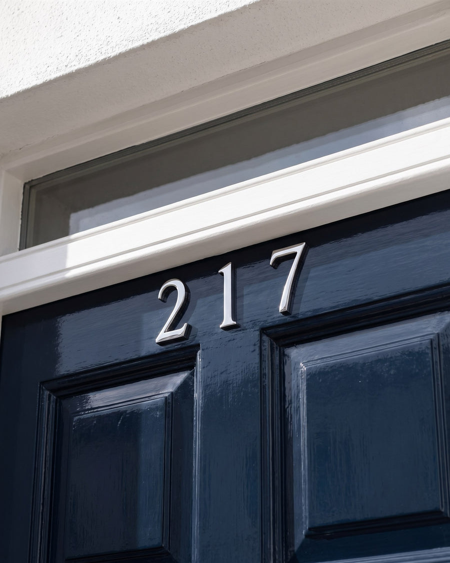 Polished chrome house numbers on the top rail of a navy gloss front door beneath the fanlight