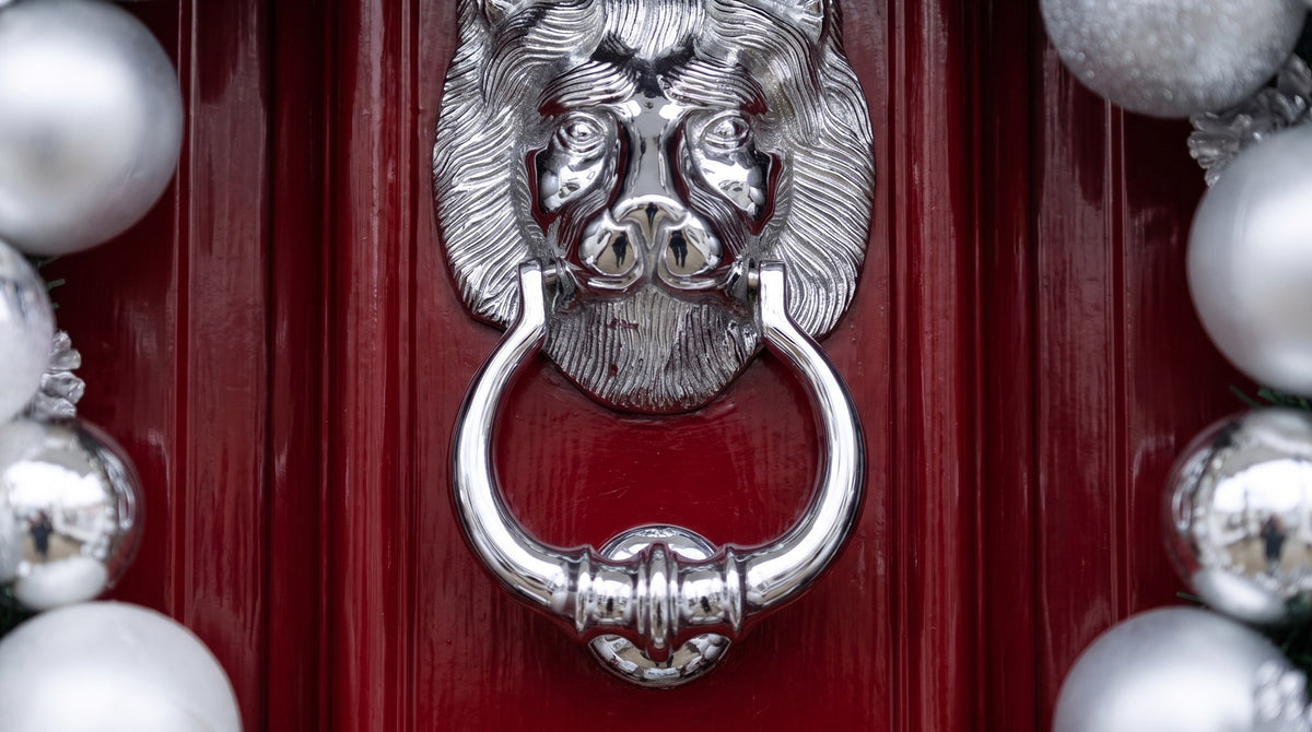Polished chrome lion head door knocker with its ring, centred in a wreath of silver and white baubles on a glossy lacquer-red front door