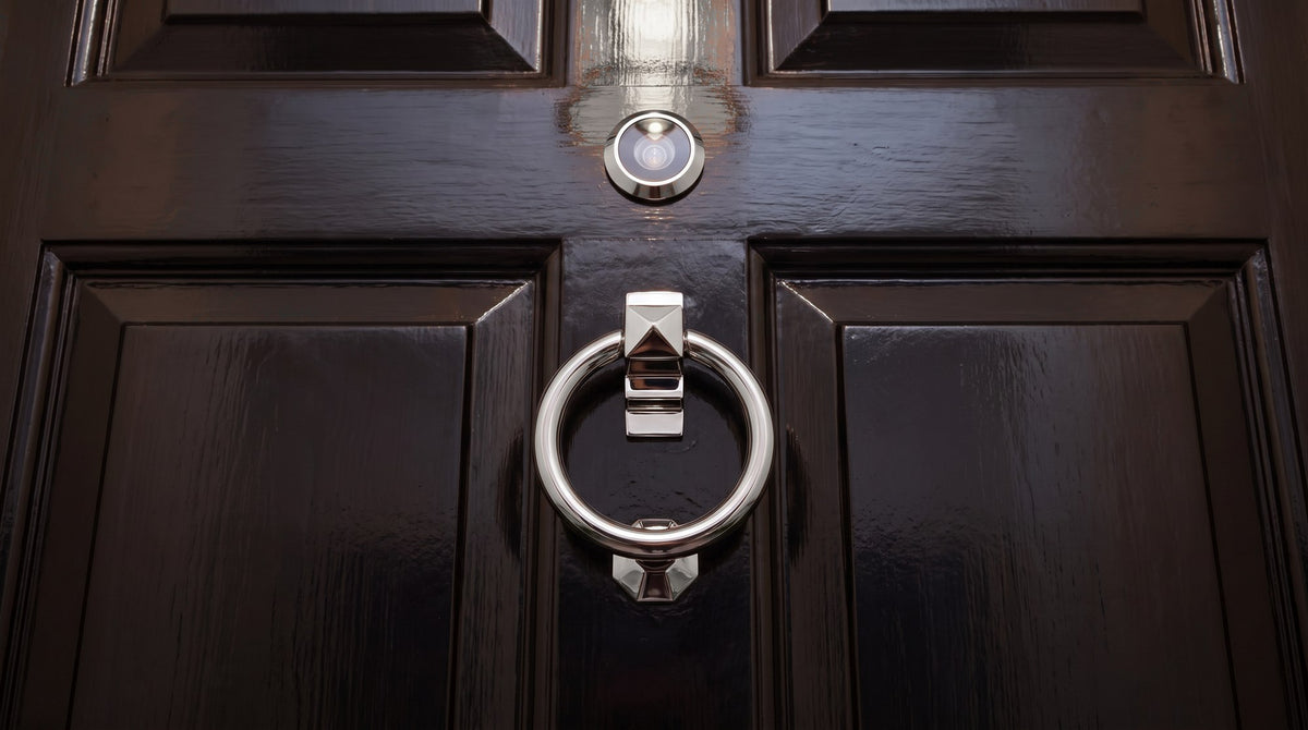 Polished chrome ring knocker below a chrome door viewer on a glossy black panelled flat door