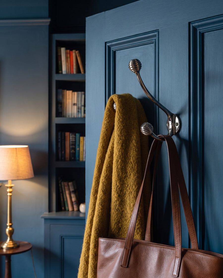 Polished nickel beehive hat and coat hook holding a mustard throw and leather tote on an ink blue door