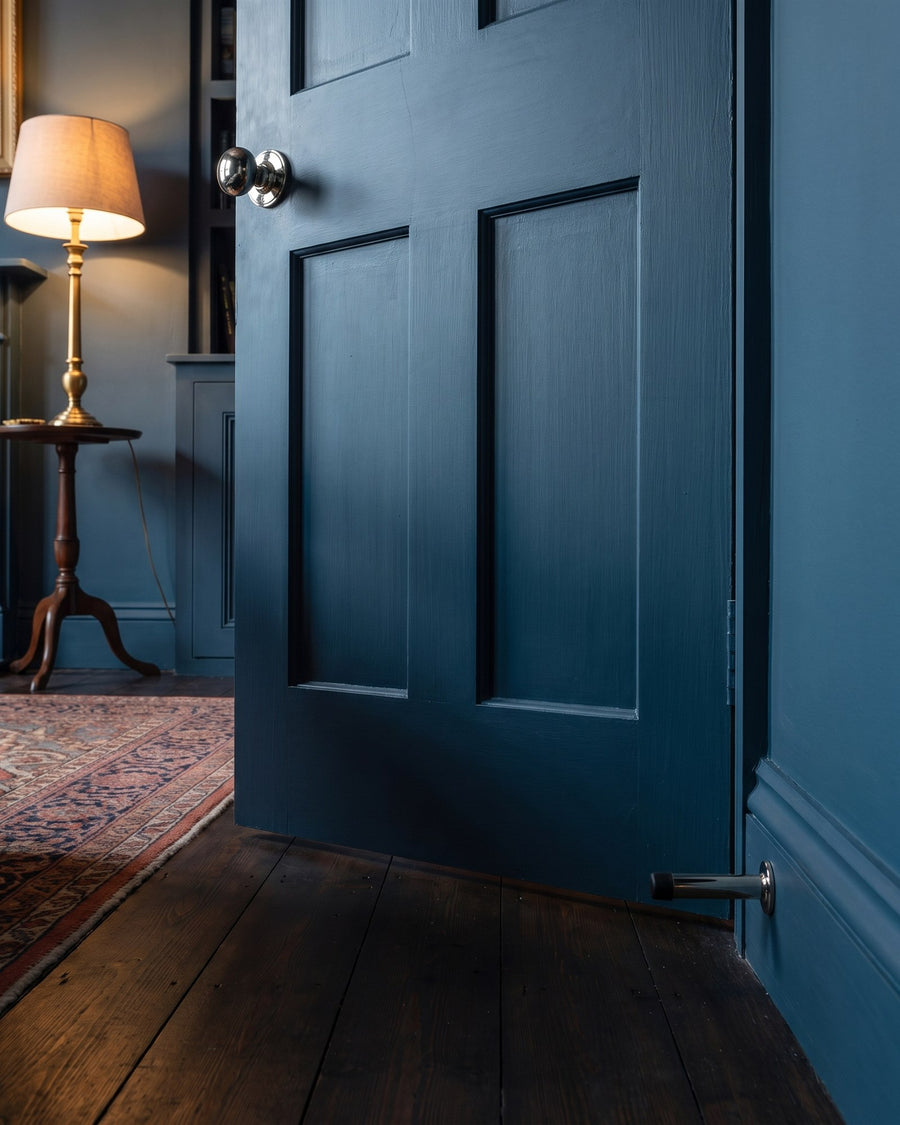 Ink blue panelled door resting against a polished nickel cylinder door stop on the ink blue skirting
