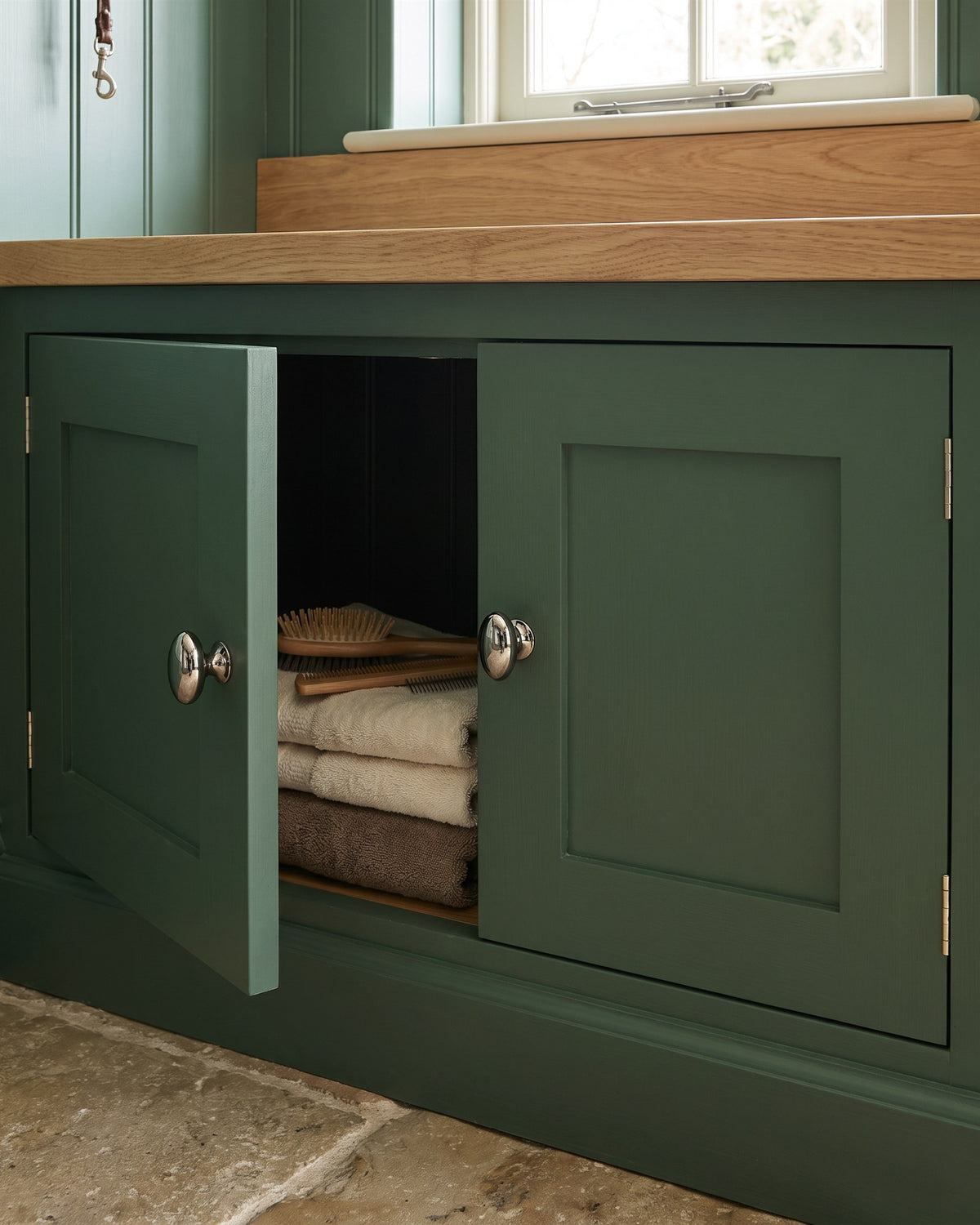 Polished nickel oval cupboard knobs on heritage green shaker cupboard doors, one open to show dog towels