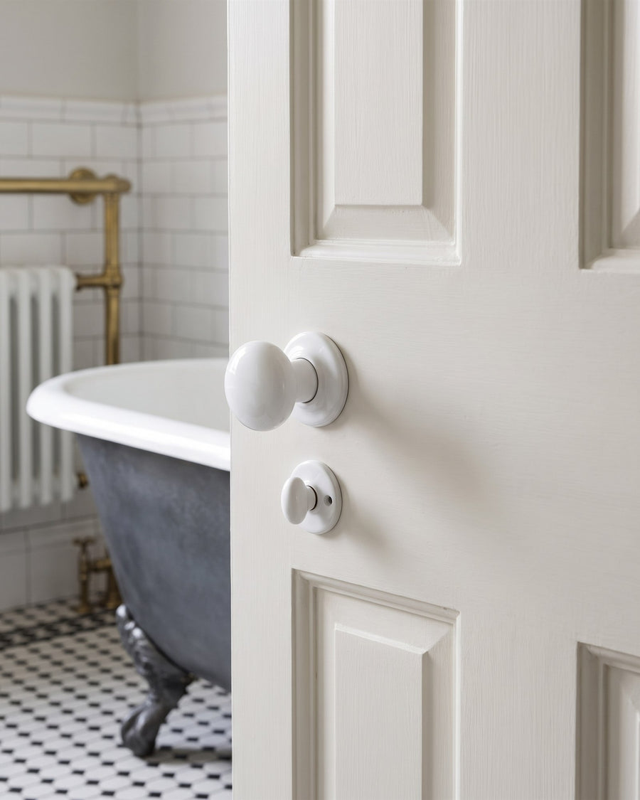 White porcelain knob with a porcelain turn and release below on a bathroom door, roll-top bath and mosaic floor beyond