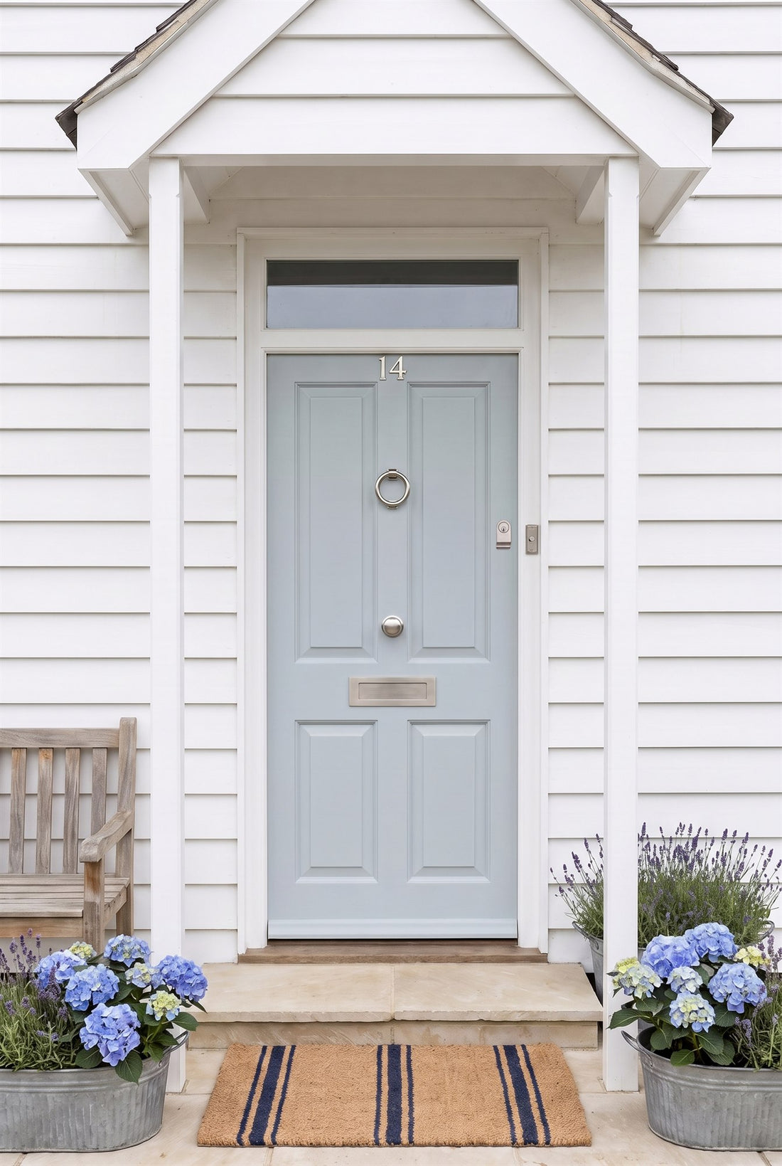 Powder blue four-panel front door on a white weatherboard house with satin nickel numbers, ring knocker, centre knob, letter plate, cylinder pull and bell push under a white porch