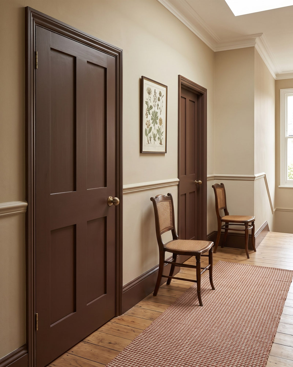 Edwardian hallway with putty walls, a dado rail, oak floor, a rust runner, cane chairs and chocolate brown panelled doors with antique brass knobs