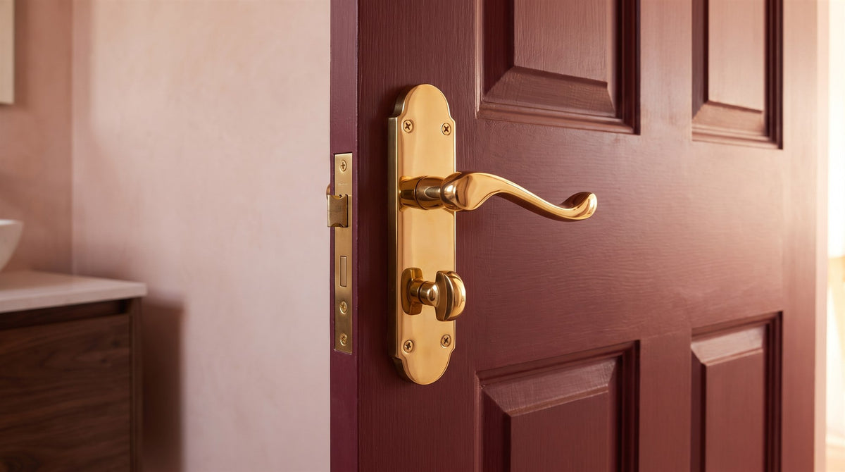 PVD brass Oakley scroll bathroom handle and turn on a deep burgundy en suite door, with blush micro-cement walls behind