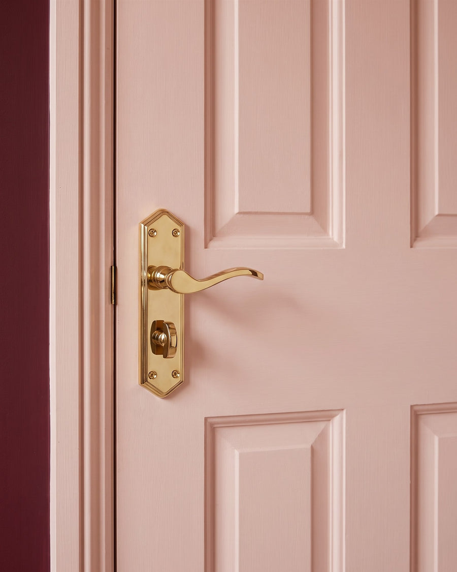 PVD brass Paris bathroom handle with clipped-corner backplate, scroll lever and turn on a blush pink panelled door
