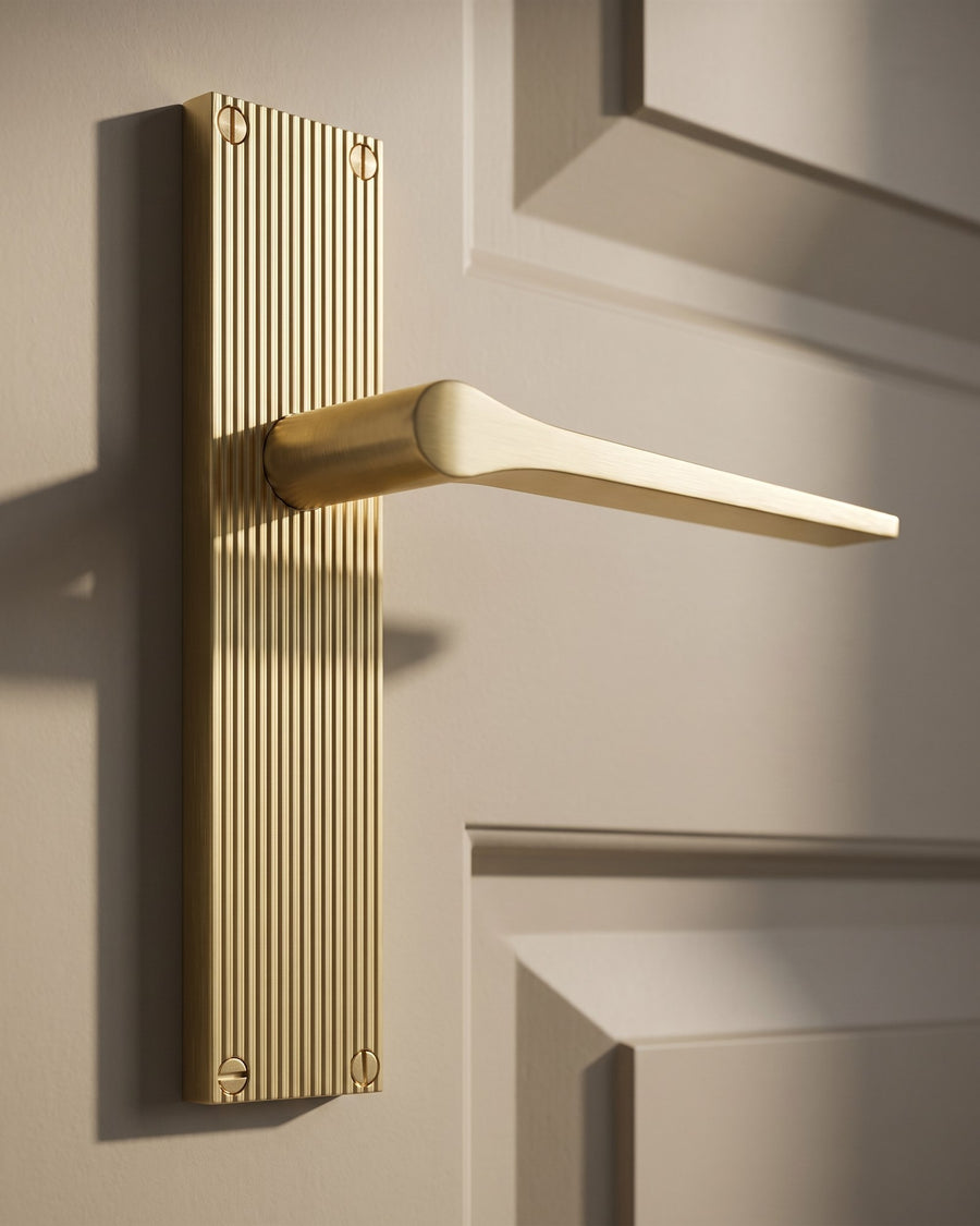 Close-up of a satin brass Gio reeded lever handle on a putty painted door, side light picking out the reeded backplate