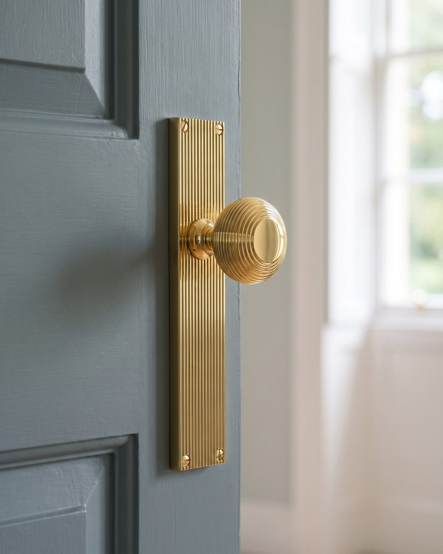 Polished brass beehive door knob on a reeded backplate on a blue-grey painted door