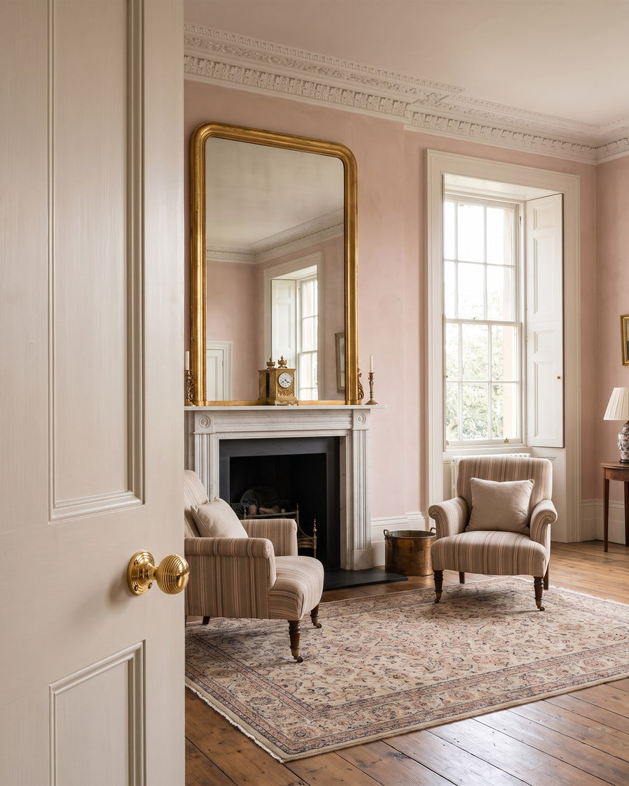 Regency drawing room with plaster pink walls, a gilt mirror and marble fireplace, seen past an off-white six-panel door with a polished brass reeded knob