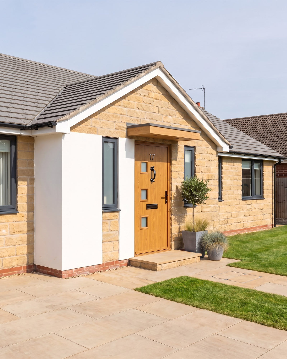Renovated 1960s bungalow with sandstone cladding, a white render panel, anthracite windows and a golden oak composite door under an oak canopy