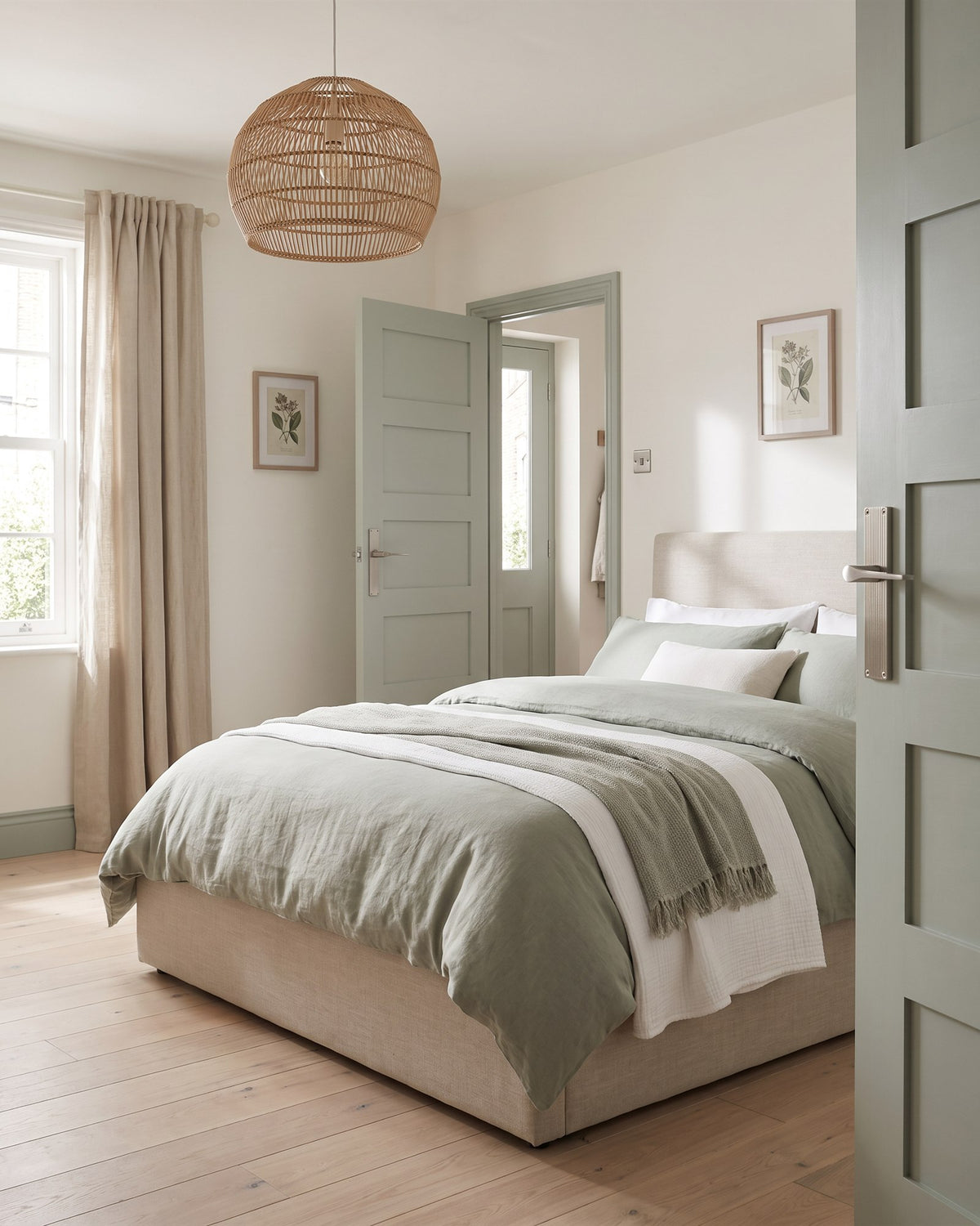 Calm bedroom with sage and white linen bedding, a rattan pendant and botanical prints, a sage door with a satin nickel lever on a reeded plate