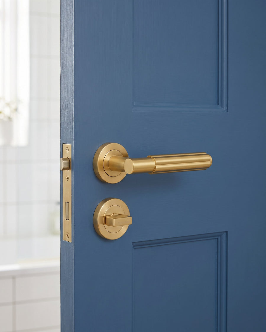 Satin brass Bloom reeded lever above a satin brass turn and release on a mid-blue bathroom door