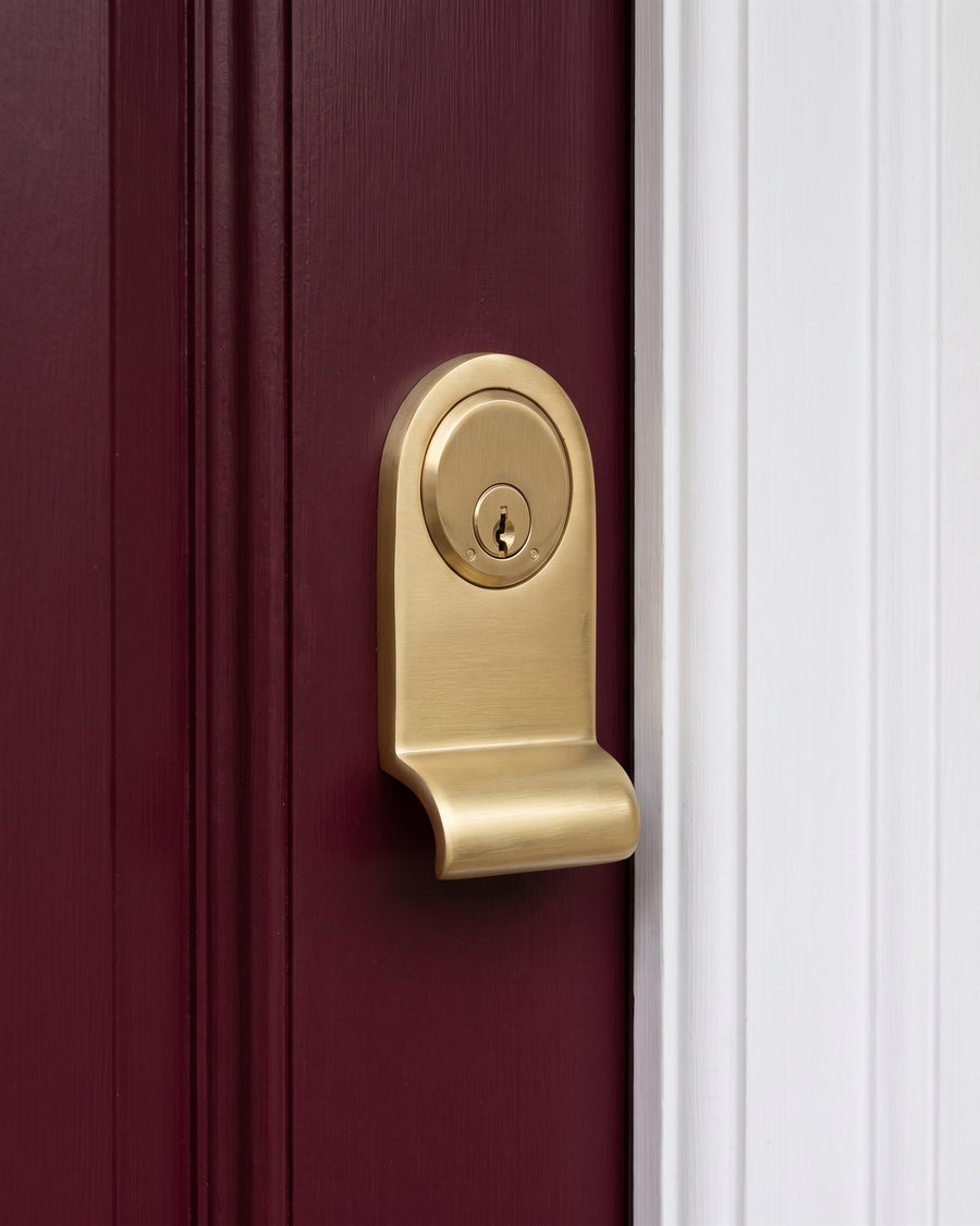 Satin brass cylinder pull with key cylinder on the edge of a burgundy front door beside a white frame