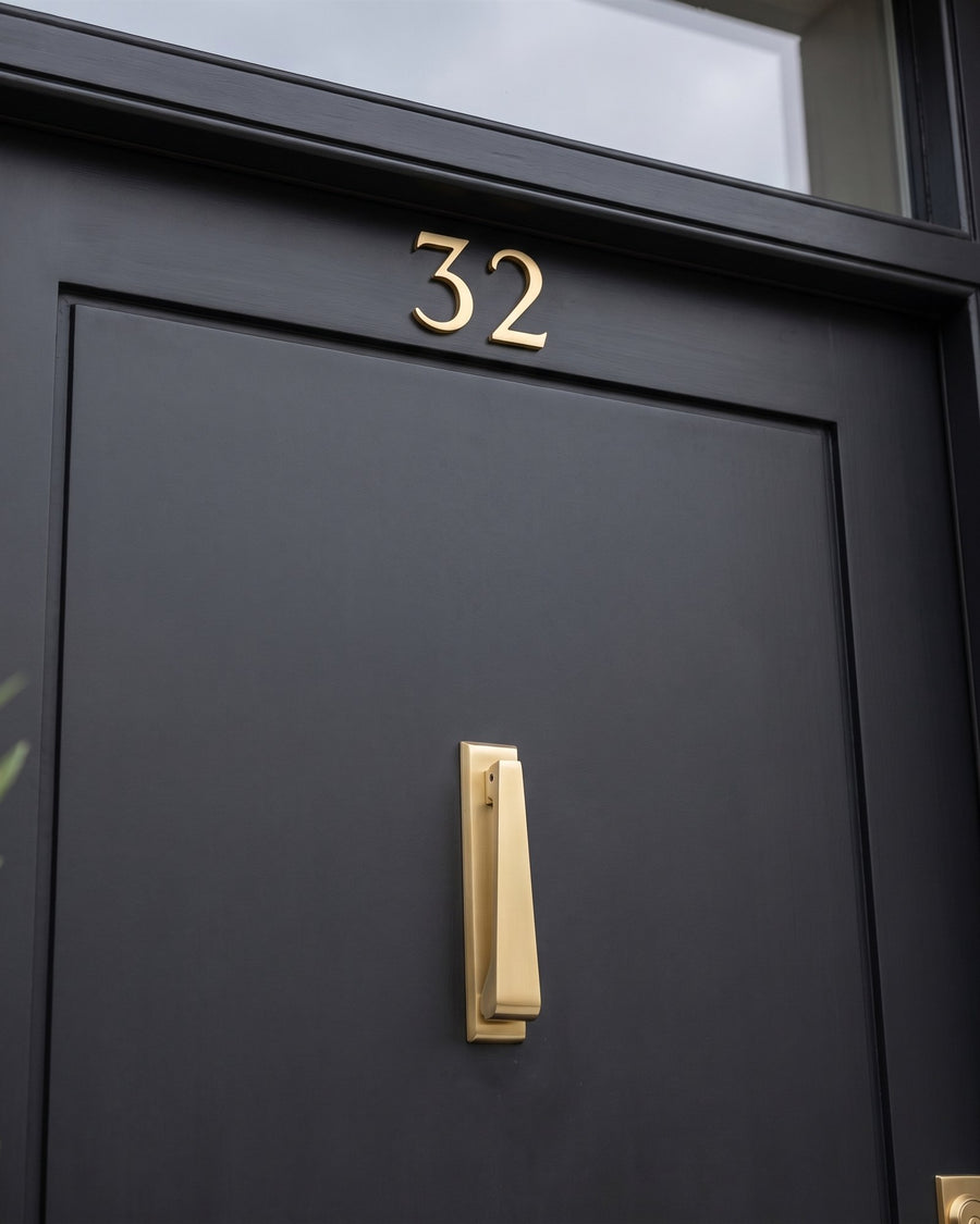 Satin brass house numbers 32 above a slim satin brass drop knocker on a matt near-black front door