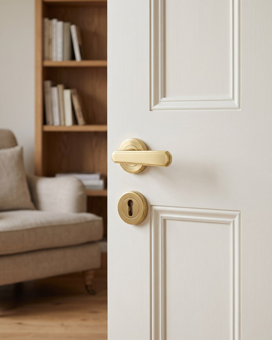 Satin brass lever on rose with a matching round keyhole escutcheon on a study door, oak bookshelves and a linen armchair behind