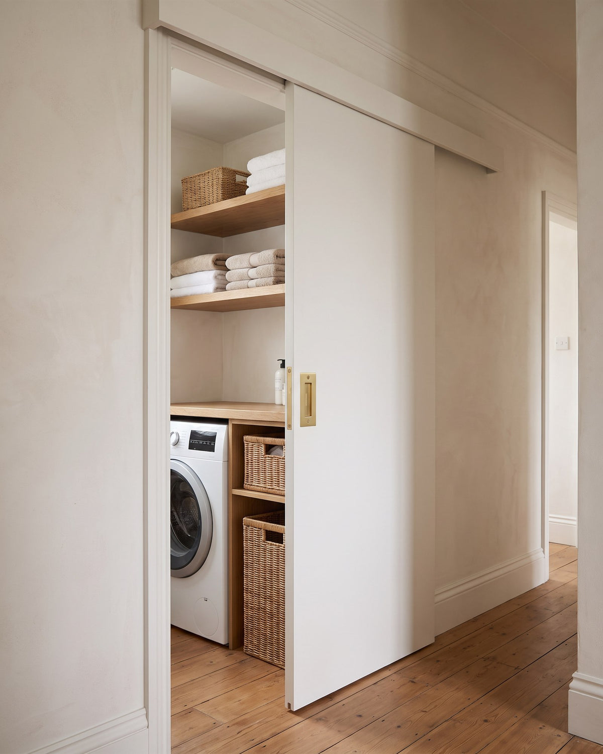 White sliding door on a top track half open on a laundry cupboard, with a satin brass rectangular flush pull