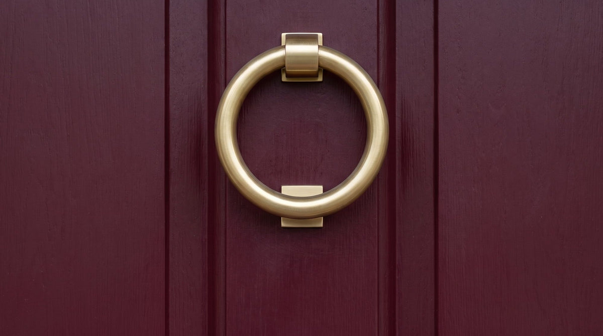 Satin brass ring door knocker and stepped centre knob on a deep burgundy front door