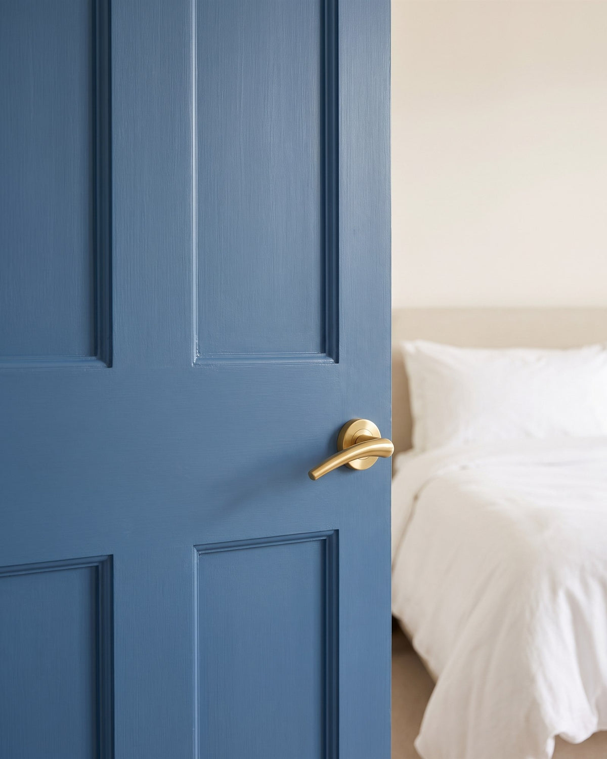Satin brass Wing lever on rose on a mid-blue bedroom door opening onto a white linen bed
