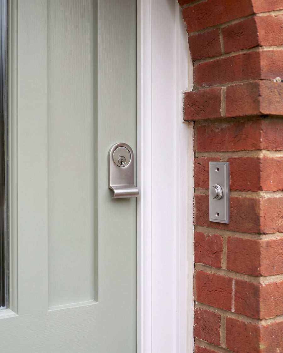 Satin chrome cylinder pull with a silver euro cylinder on a sage door beside a satin chrome stepped bell push on the brick porch