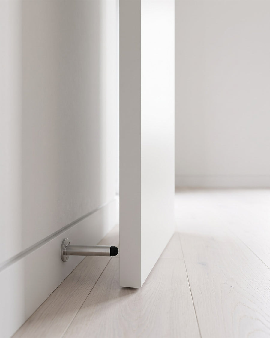 Flush white door resting on a satin chrome projecting door stop above a shadow-gap skirting and pale oak floor