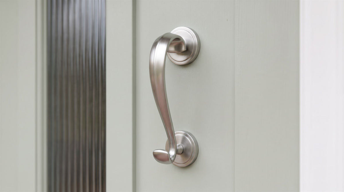 Satin chrome Sloane scroll knocker with its curved bar and hooked tail on a soft sage green front door