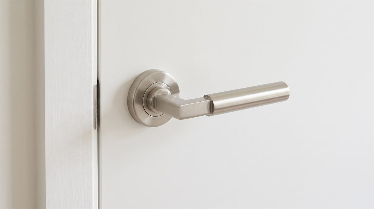 Satin nickel Bauhaus lever with a flat square arm turning into a round grip, on a round rose on a warm white door