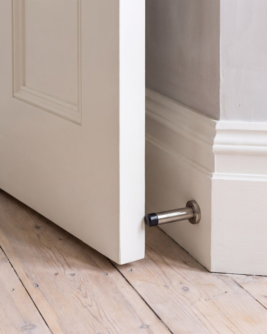 Warm white door resting on a satin nickel cylinder door stop on a deep skirting above limed pine boards