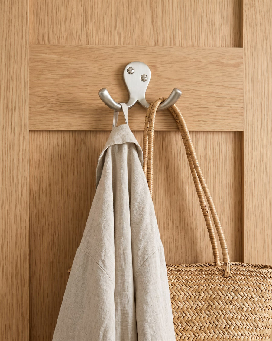 Satin nickel double coat hook holding a linen dressing gown and a rattan bag on the back of an oak veneer door