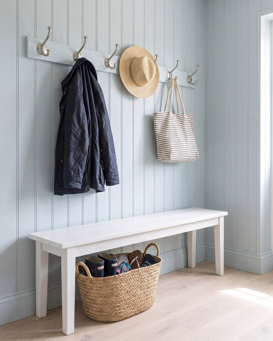 Satin nickel hat and coat hooks holding a navy jacket, straw hat and beach bag in a blue tongue-and-groove boot room