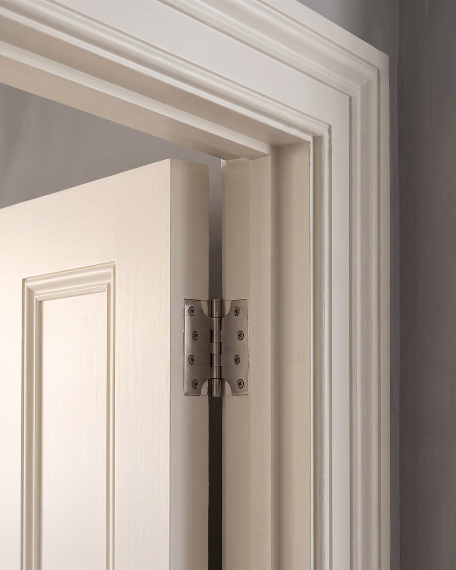 Satin nickel parliament hinge holding a warm white panelled door clear of a deep moulded architrave