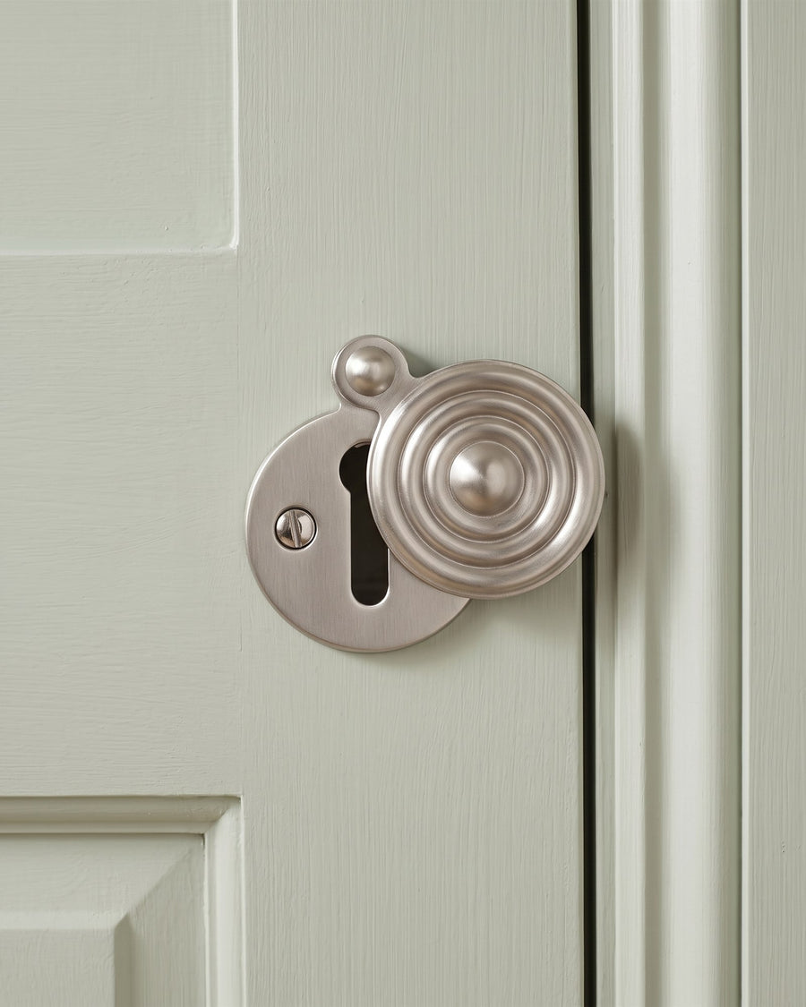 Satin nickel reeded covered escutcheon over an old keyhole on a sage painted door