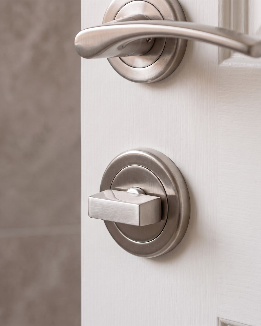 Satin nickel turn and release on a round rose below a curved Sophia lever on rose, on the inside of a white en-suite door