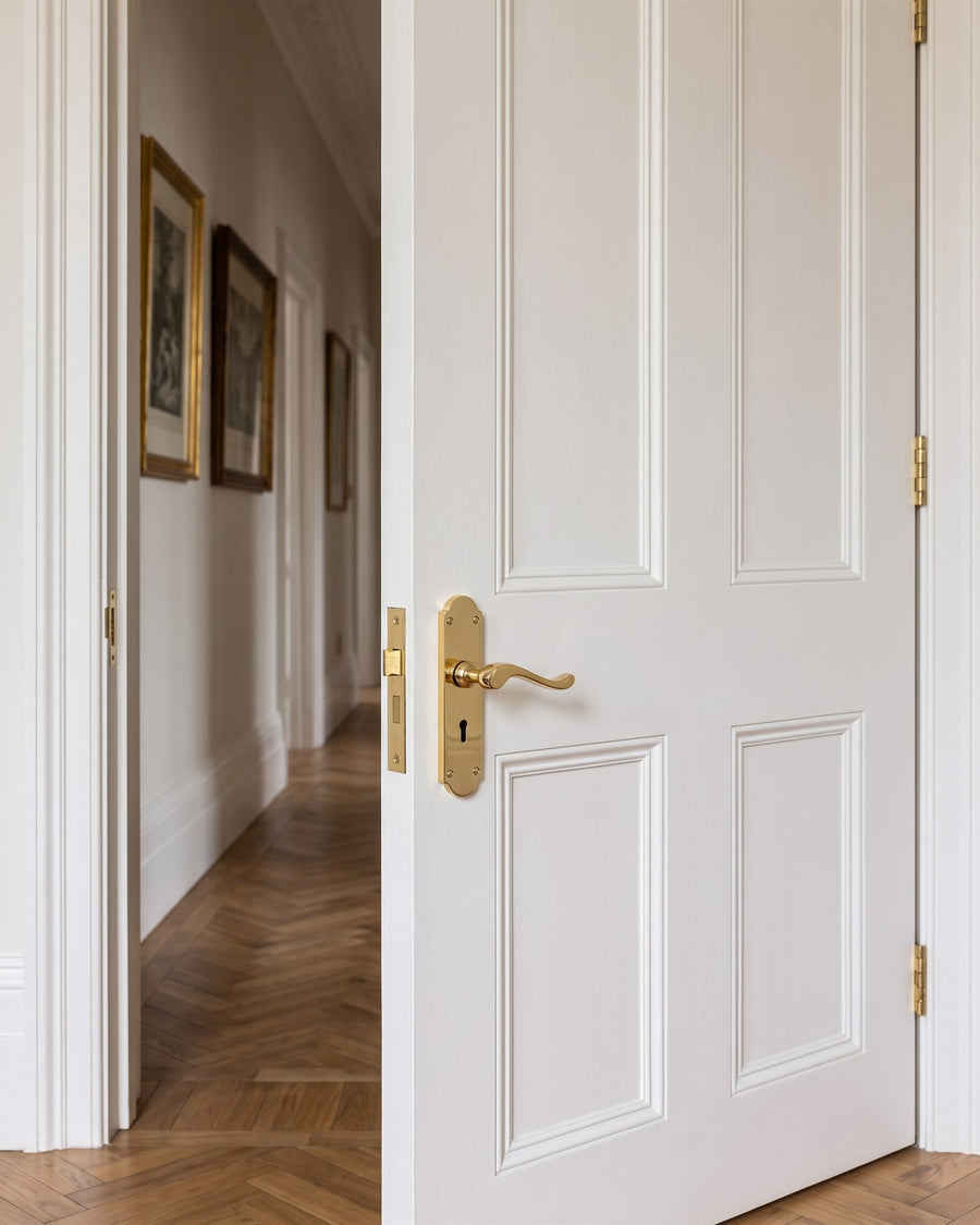 Polished brass Savoy scroll lever keyhole handle on a tall white panelled door opening onto a parquet corridor