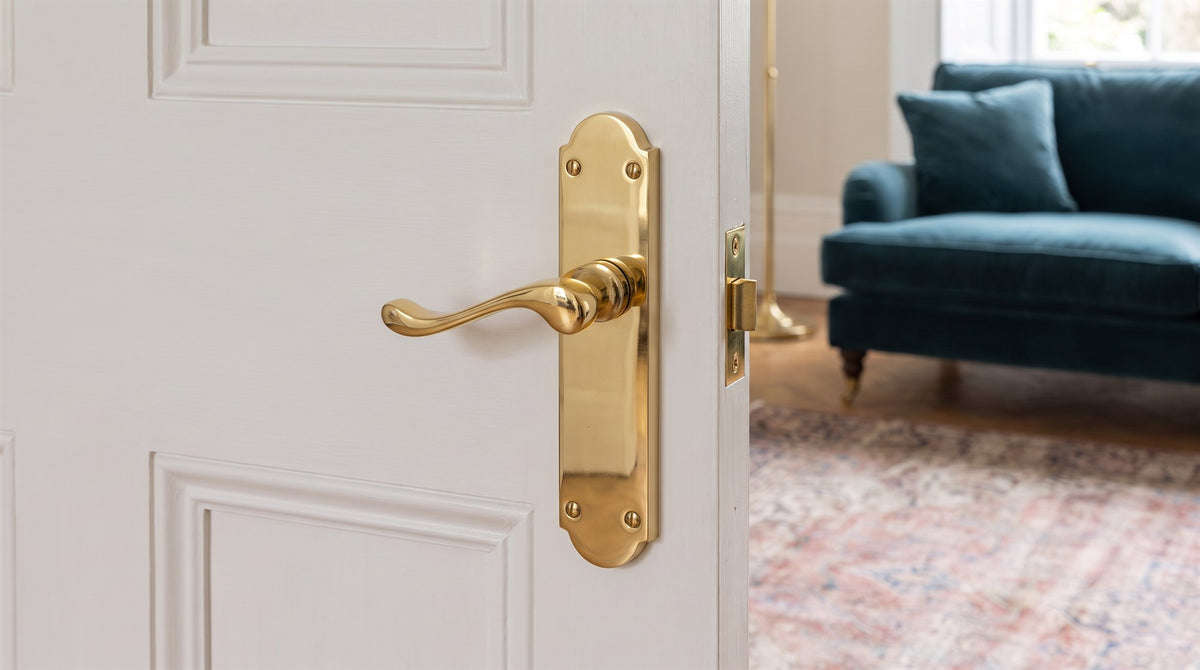 Polished brass Savoy scroll lever on a tall arched backplate on a white panelled door in an Edwardian flat