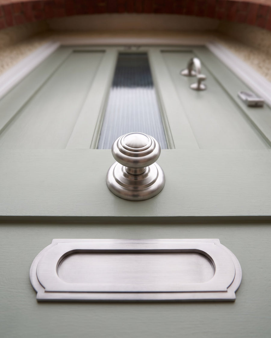 Satin chrome Sloane stepped centre knob above a Sloane letter plate with scalloped ends on a sage green door