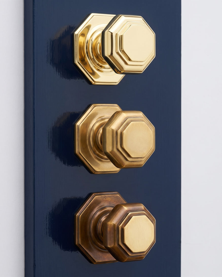 Three unlacquered brass octagonal centre knobs on a navy board showing how the finish ages: bright when new, mellow after six months and a deep warm patina after two years