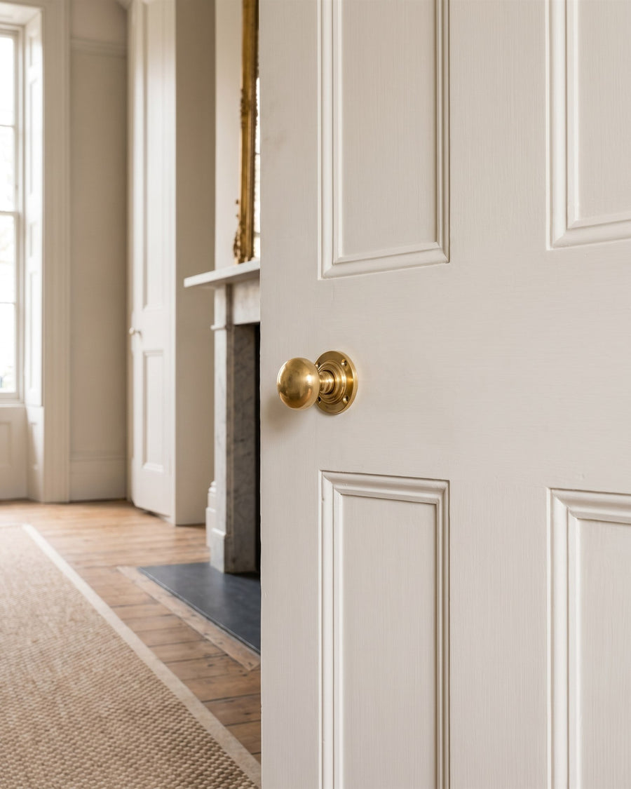 Unlacquered brass mushroom mortice knob on a chalky off-white six-panel door in a Georgian drawing room