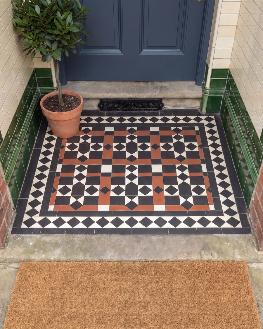 Black, white and terracotta encaustic tiled porch floor with a cast-iron boot scraper in the stone step, green and cream glazed wall tiles and a potted bay