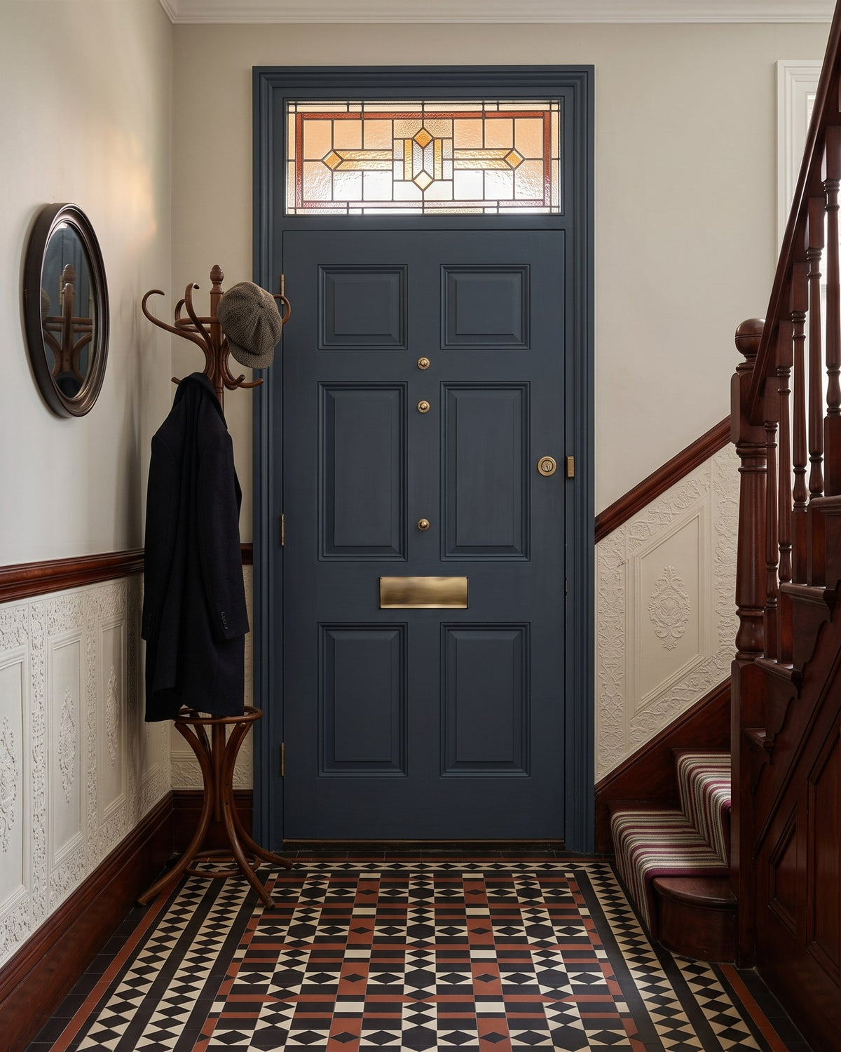 Victorian hallway with an encaustic tiled floor, Lincrusta dado and mahogany staircase, looking at the inside of the grey front door with its antique brass interior flap