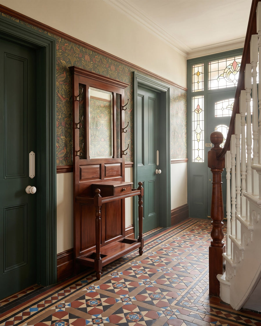 Victorian hall with encaustic floor tiles, patterned wallpaper, a mahogany hall stand and deep green doors with white porcelain knobs and finger plates