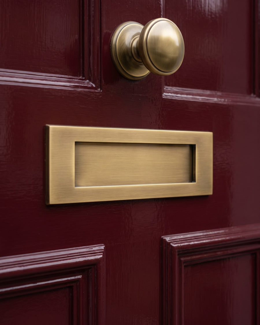 Antique brass letter plate on the middle rail of a gloss oxblood door with the centre knob above