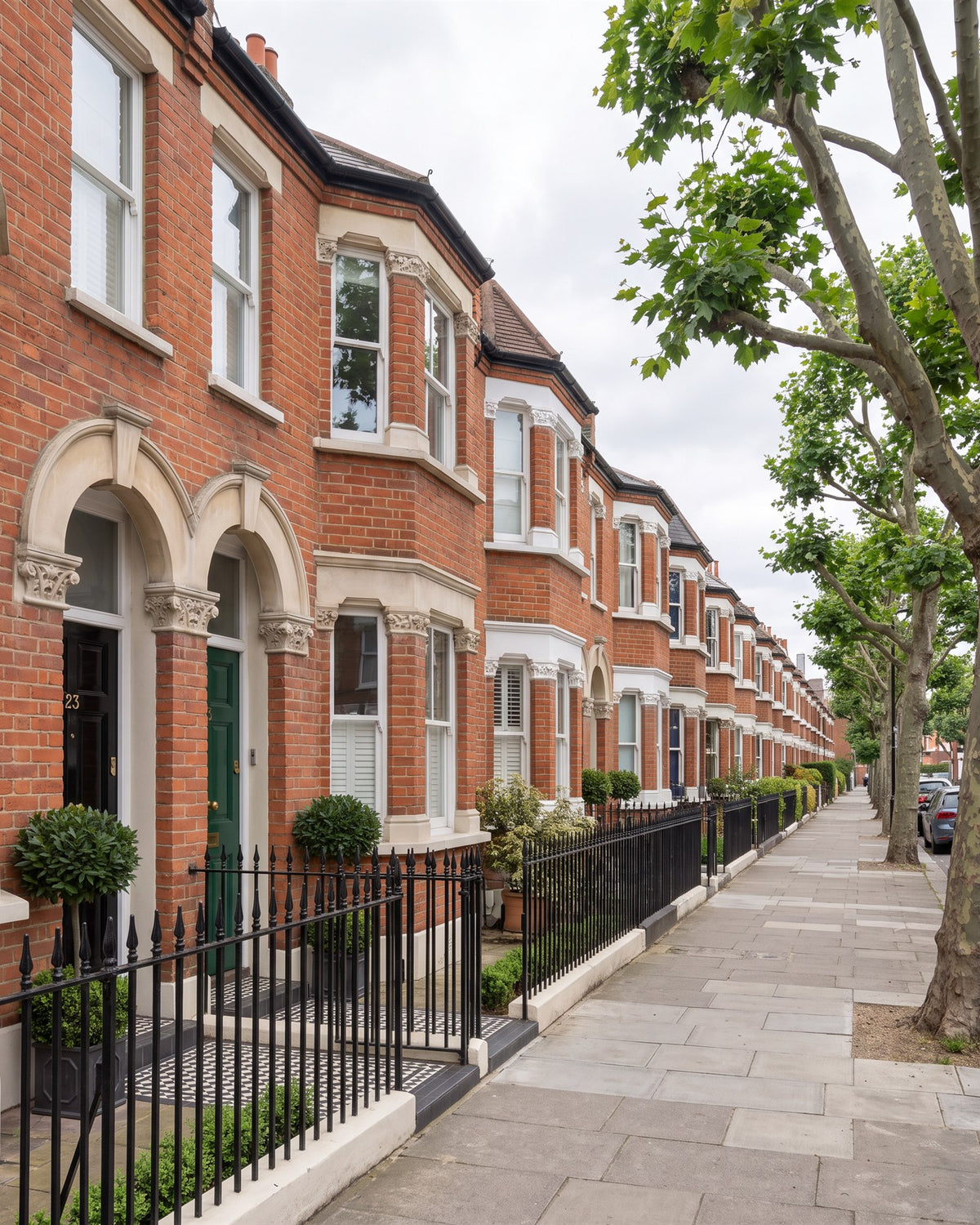 Victorian red-brick terrace street with stone arched porches, bay windows, black railings and plane trees, the front doors painted black, green and other colours