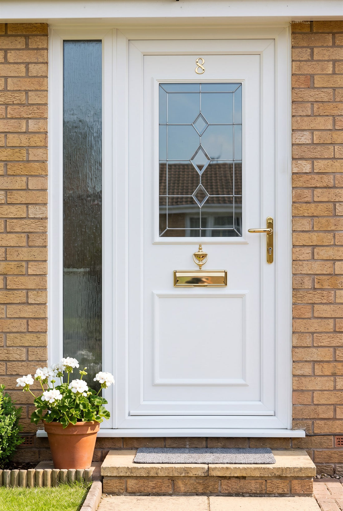 White uPVC front door with a leaded glass panel and patterned side light in buff brick, fitted with Hardex gold number 8, urn knocker, Nu Mail shield letter plate and Windsor lever handle